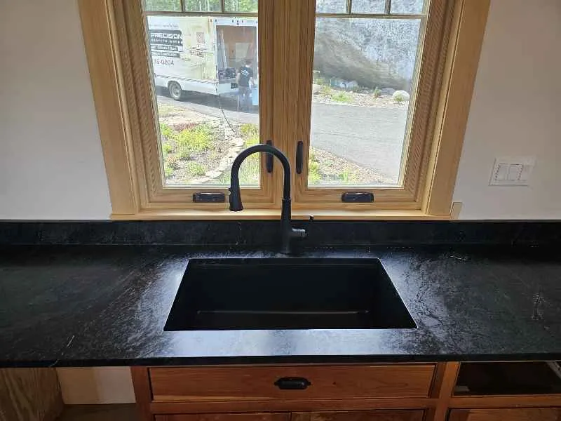 Black soapstone countertop with an undermount sink and matte black faucet in a New Hampshire kitchen