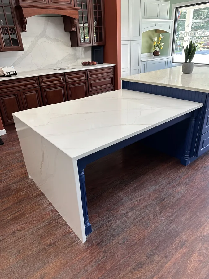 White quartz waterfall island with navy cabinetry at the Precision Granite Works showroom in Epsom New Hampshire